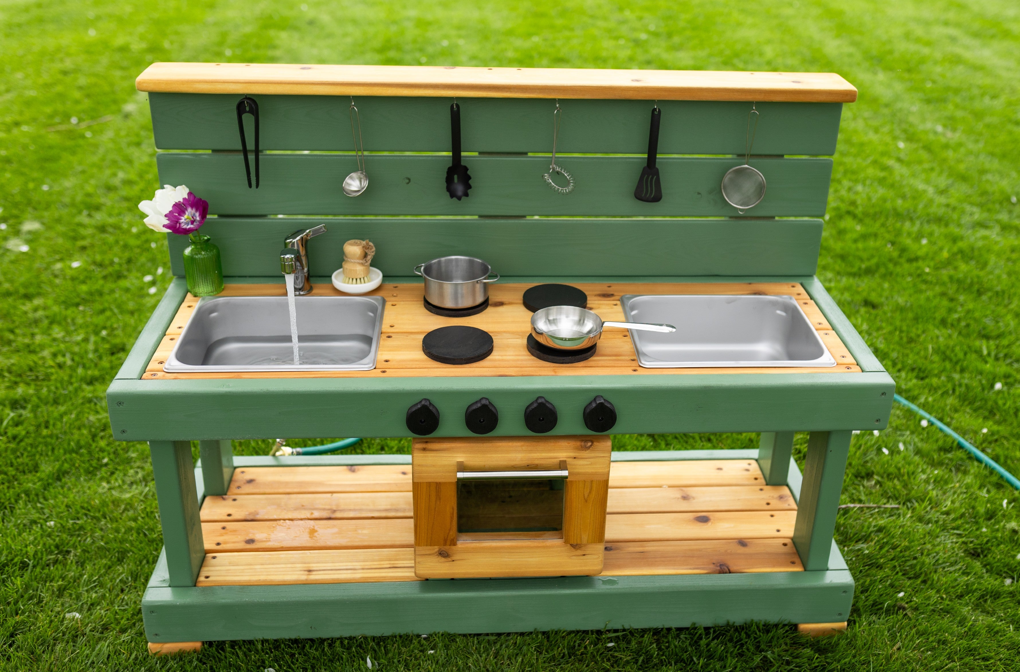 Green wooden mud kitchen with two sinks and a toy oven.